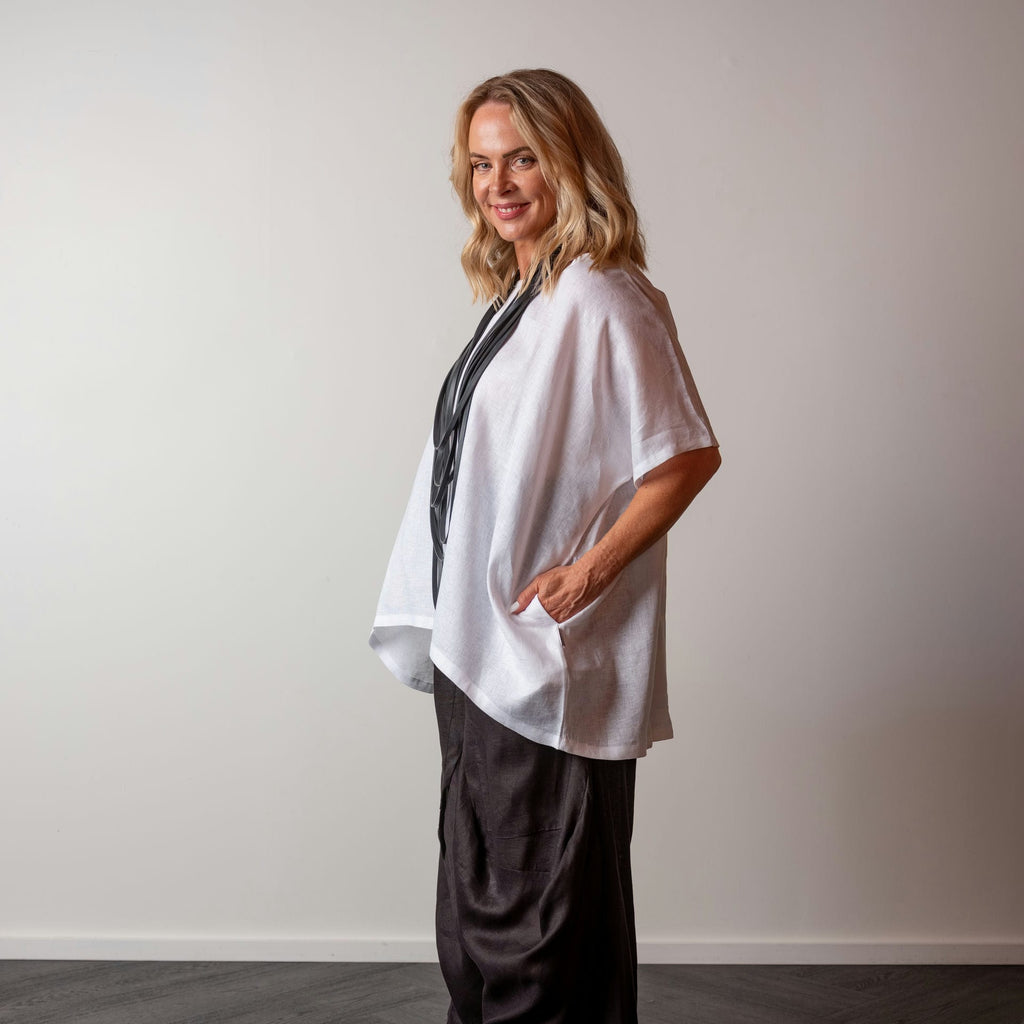 Woman wearing a white linen top and dark pants against a plain background